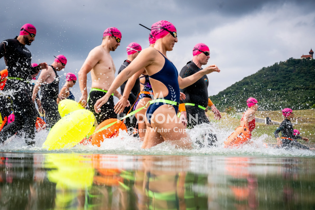 Start of the 3 km race at HYDROMAN Most Swim – swimmers run into the water with Hněvín Castle in the background. Action shot from open water swimming in Most.